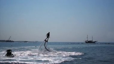 Flyboard denizin üzerinde eğleniyor bir adam silüeti.