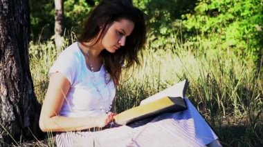 Güzel genç kız açık havada bir kitap okuyor.