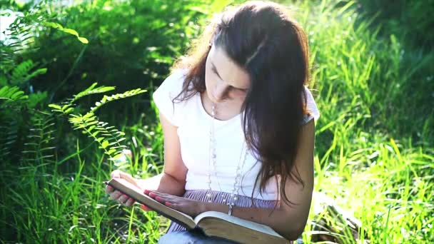Beautiful young girl is reading a book outdoors. — Stock Video