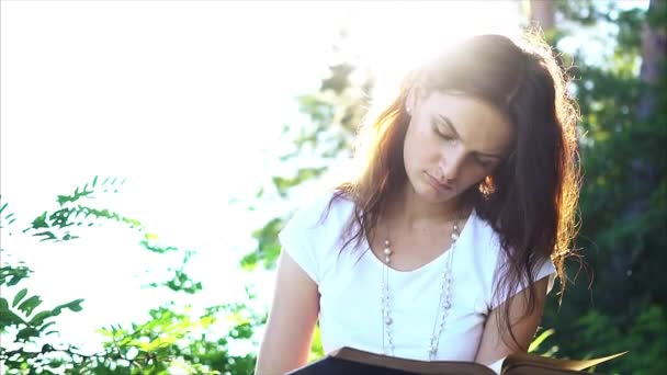 Hermosa joven está leyendo un libro al aire libre . — Vídeos de Stock