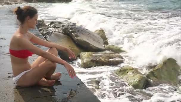 Chica se sienta en el muelle de hormigón y observa las olas . — Vídeos de Stock