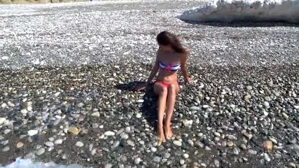 Lány ül a strandon, és egyre lába nedves miatt egy hullám — Stock videók