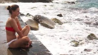 Kız beton iskelede oturur ve dalgalar gözlemler.