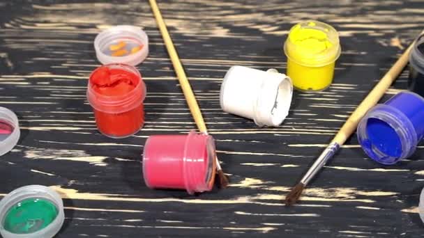 Een heleboel varicolored verf gouache potten met borstels op houten achtergrond — Stockvideo