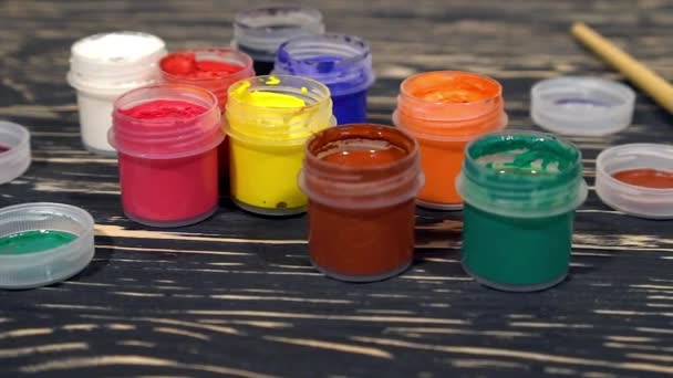 A lot of varicolored paint gouache jars with brushes on wooden background — Stock Video