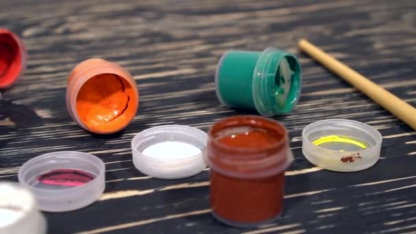 A lot of varicolored paint gouache jars with brushes on wooden background — Stock Video