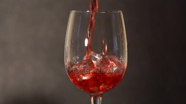 Kırmızı içecek bir bardak içinde eriyen buz küpleri.