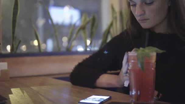 Close up portrait of young woman using her smart phone and drinking coctail. — Stock Video