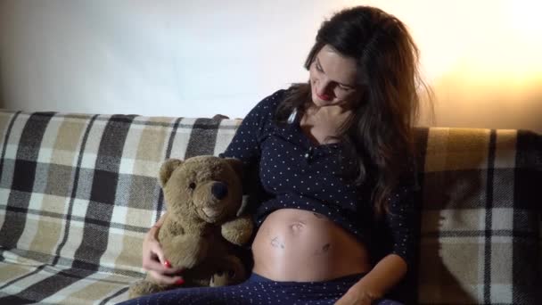 Счастливая беременная женщина отдыхает на диване и гладит животик. . — стоковое видео
