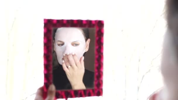 Jonge vrouw doet gezichtsmasker blad met zuiveren masker op haar gezicht. — Stockvideo