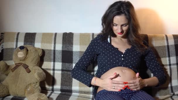 Glad gravid kvinna vilar på en soffa och strök hennes mage. — Stockvideo