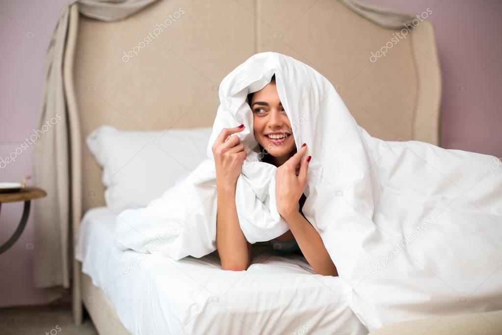 Young woman hiding under blanket.