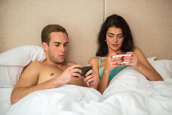 Pareja con teléfonos en la cama. —  Fotos de Stock