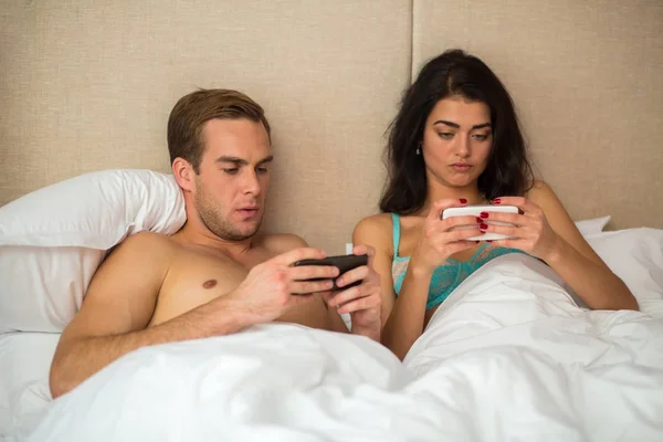 Paar im Bett mit Telefonen. — Stockfoto