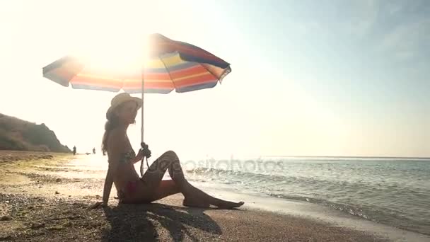 Señora sentada cerca de la sombrilla de playa . — Vídeos de Stock