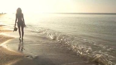 Güneşli sahil üzerinde yürüyen kadın.