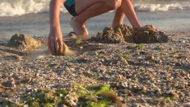 Парень на берегу моря копает яму . — стоковое видео