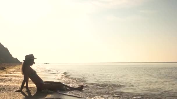 Mujer con sombrero sentada, orilla del mar . — Vídeo de stock