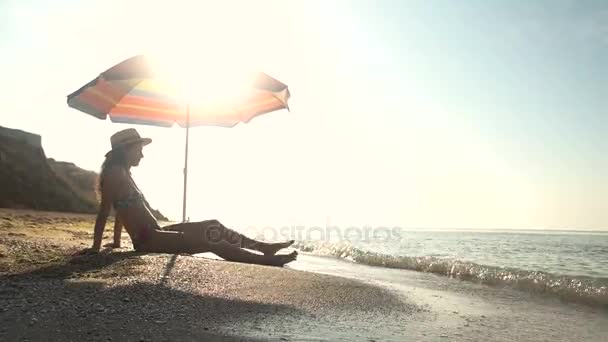 ビーチ パラソルの近くに座っている女性. — ストック動画