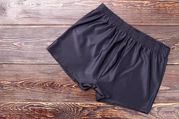 Black running shorts, wooden background.