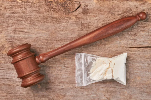 Packet of drugs, gavel, wooden background.
