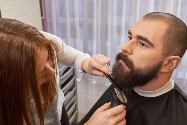 Barber woman grooming beard.