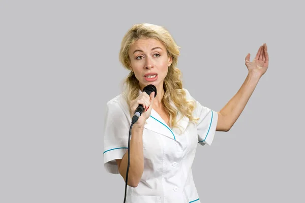 Enfermera joven gesticulando sosteniendo micrófono . — Foto de Stock