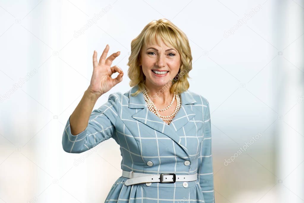 Smiling mature lady showing sign ok.