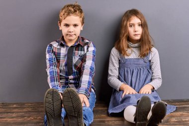 Sevimli kız ve erkek kardeş duvara yakın oturan.