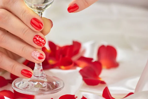Weibliche rote Maniküre und Champagnerglas. — Stockfoto