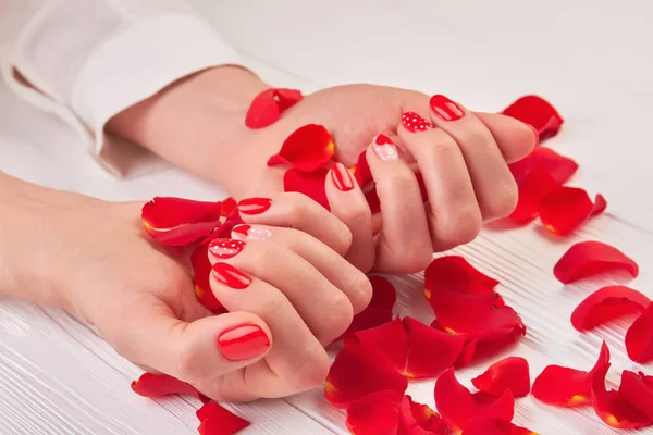 Schöne rote Maniküre und Rosenblätter. — Stockfoto