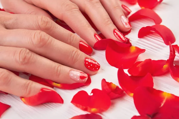Frau rote Nägel und Rosenblätter. — Stockfoto