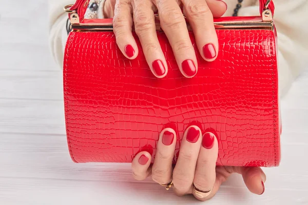 Elegant red handbag in female hands.