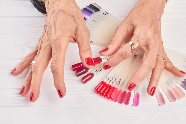 Old woman compares nail color with nail sample.
