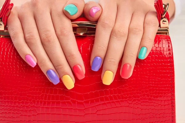 Multicolored manicure and expensive red handbag. — Stock Photo, Image