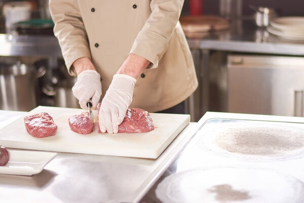 Big steak sliced on cutting board. Chef cutting big red piece of beef meat. Male chef at work, kitchen.