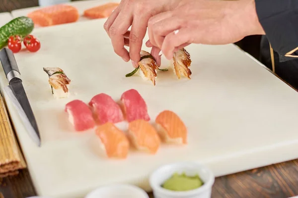 Руки шеф-повара кладут суши с угрем на белую доску . — стоковое фото