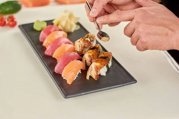 Шеф-повар держит ложку с кунжутом на суши . — стоковое фото