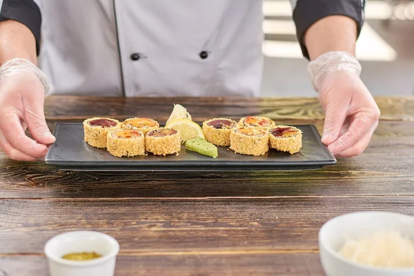 Chef manos sosteniendo plato con rollos de sushi . — Foto de Stock