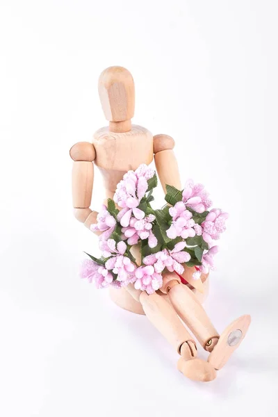 Houten pop zit met bloemen. — Stockfoto