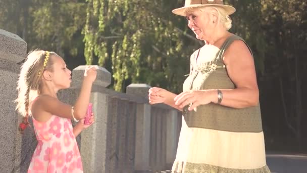 Child blowing soap bubbles to her grandmother. — Stock Video