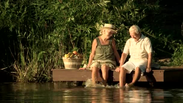 Senior couple dangling with legs in river. — Stock Video