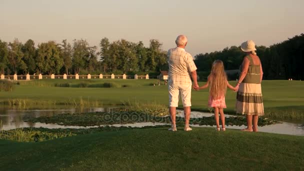 Grandparents with granddaughter walking near water. — Stock Video