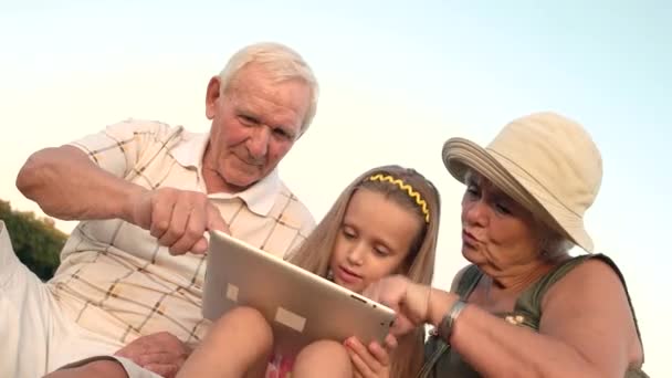 Бабушка с дедушкой и внучка играют на планшете . — стоковое видео