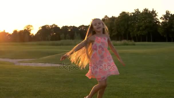 Roztomilá holčička tančí na trávě.