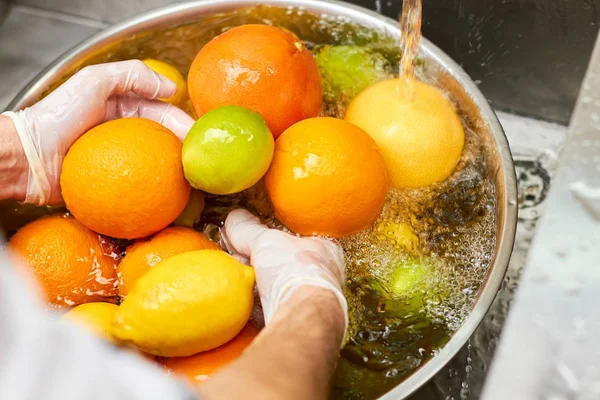 Chef washing mix of citrus fruits in a sink.