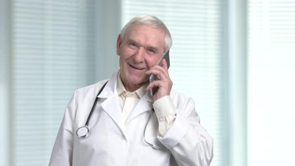 Retrato de sorrir médico de cabelo cinza sênior com smartphone . — Vídeo de Stock
