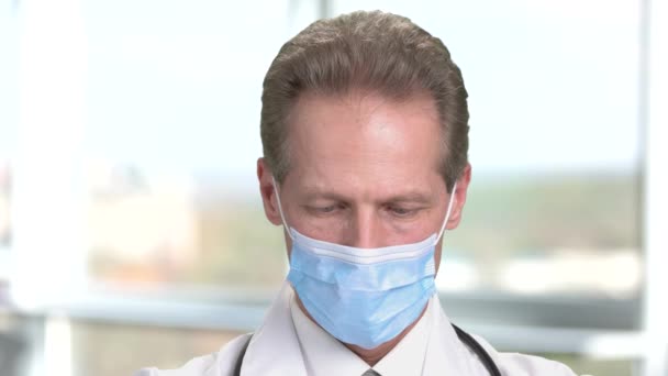 Senior doctor physician with medical mask looks down. — Stock Video