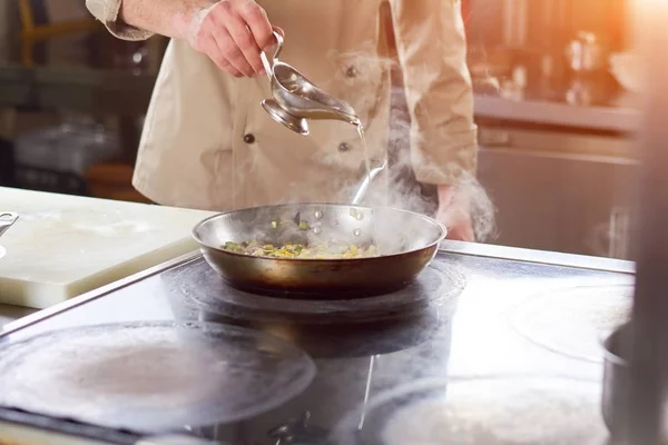 Kocken hälla olja i stekpanna med grönsaker. — Stockfoto