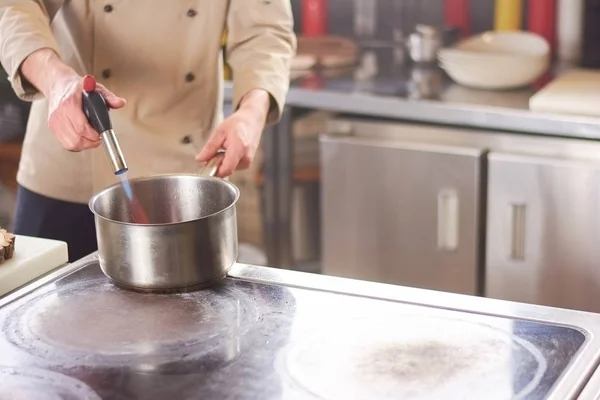 Chef burning saucepan with torch burner.